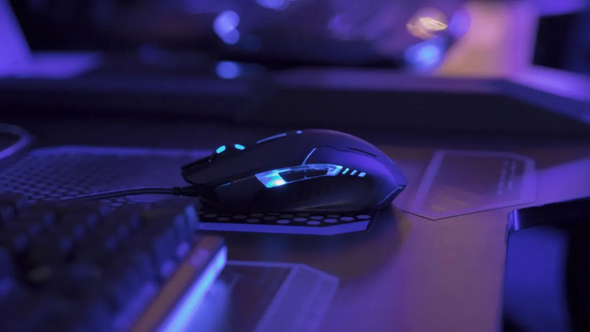 Chuột gaming có đèn trên bàn máy tính trong không gian chơi game ánh sáng xanh, biểu thị cài đặt độ nhạy chuột phù hợp.