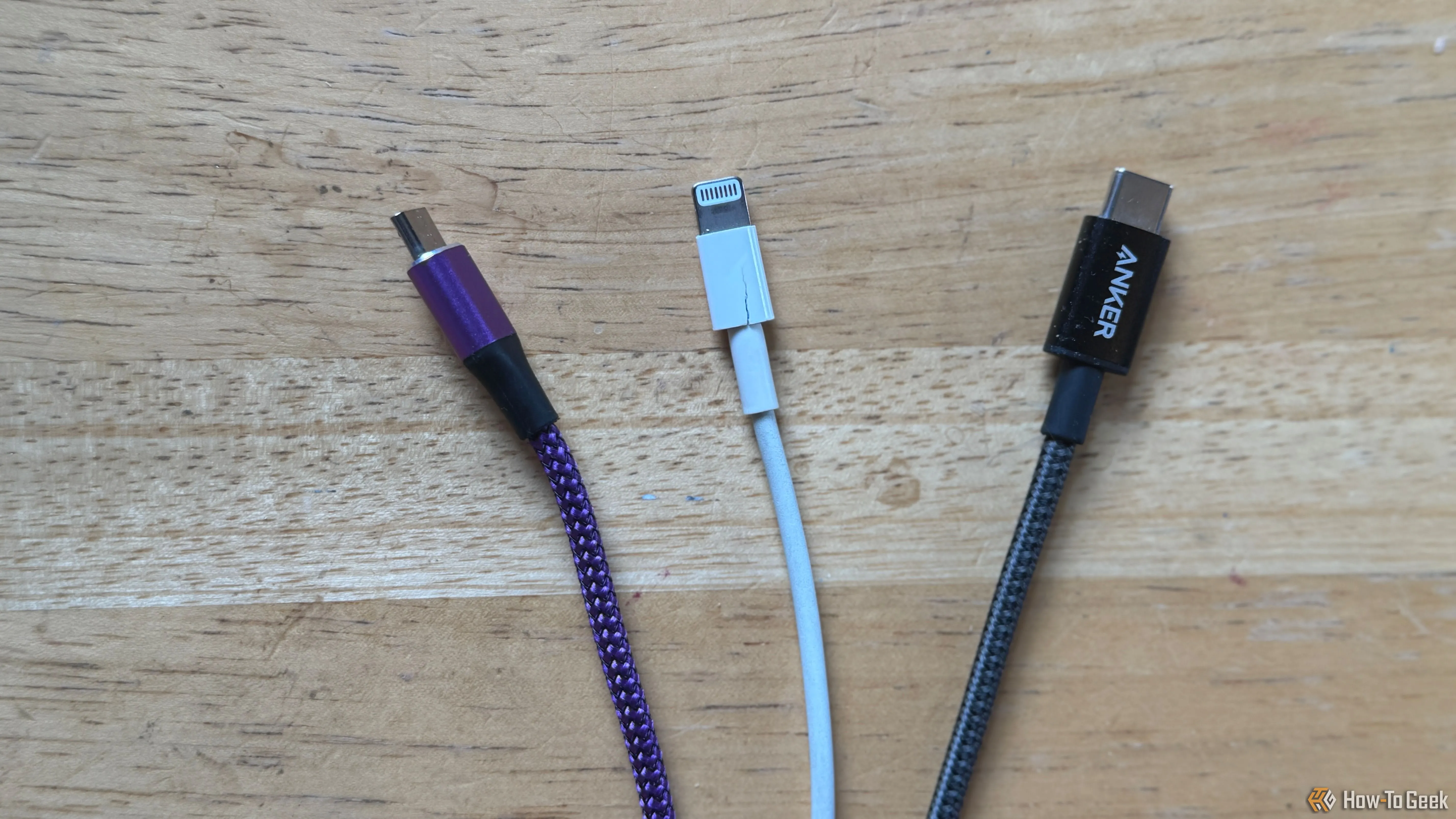 Dây cáp Micro-USB màu tím, cáp Lightning màu trắng và cáp USB-C màu xám trên bàn, minh họa cách phân biệt cáp bằng màu sắc