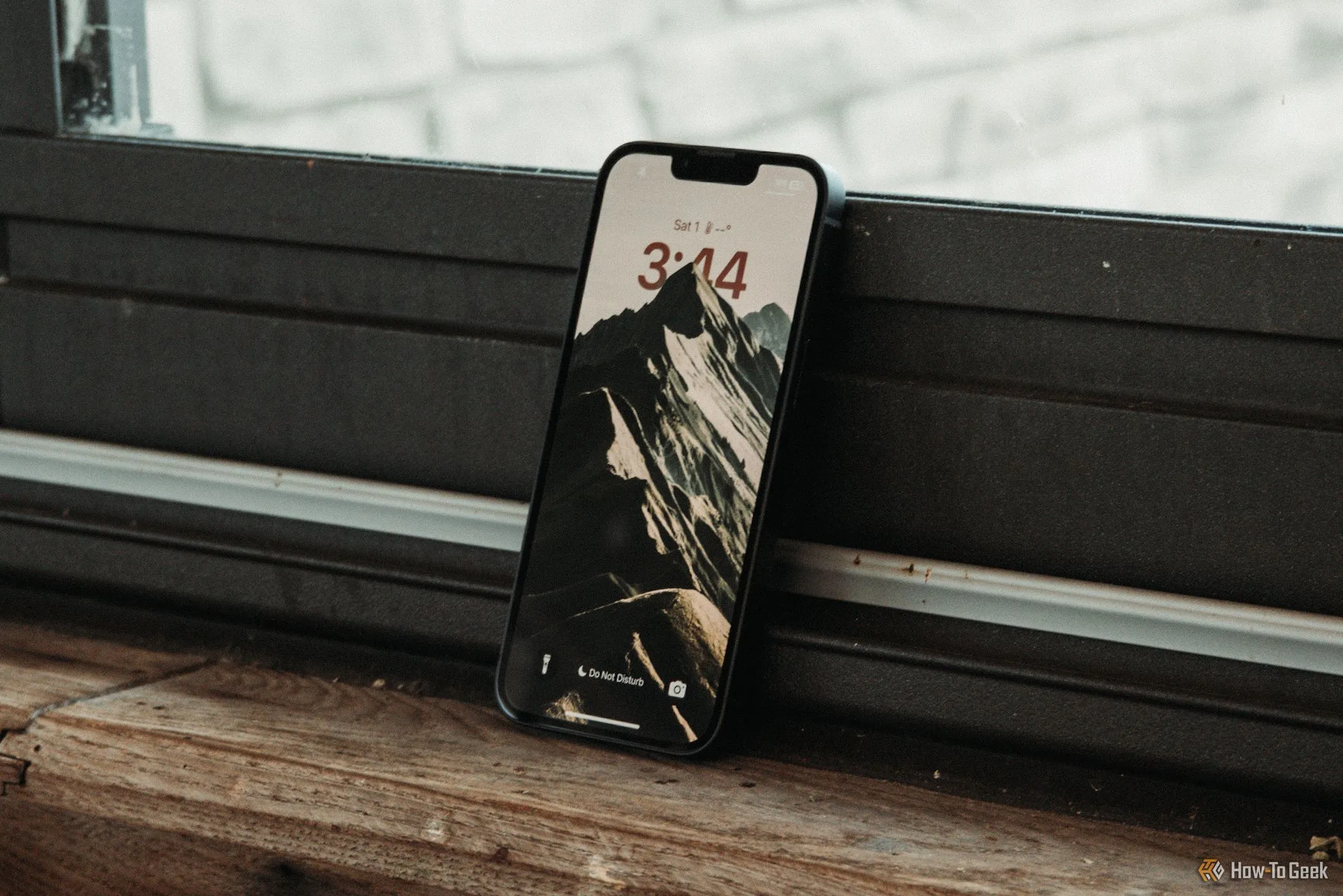 Màn hình khóa iPhone 16e hiển thị nội dung, đặt nghiêng dựa vào cửa sổ, minh họa kích thước hiển thị.
