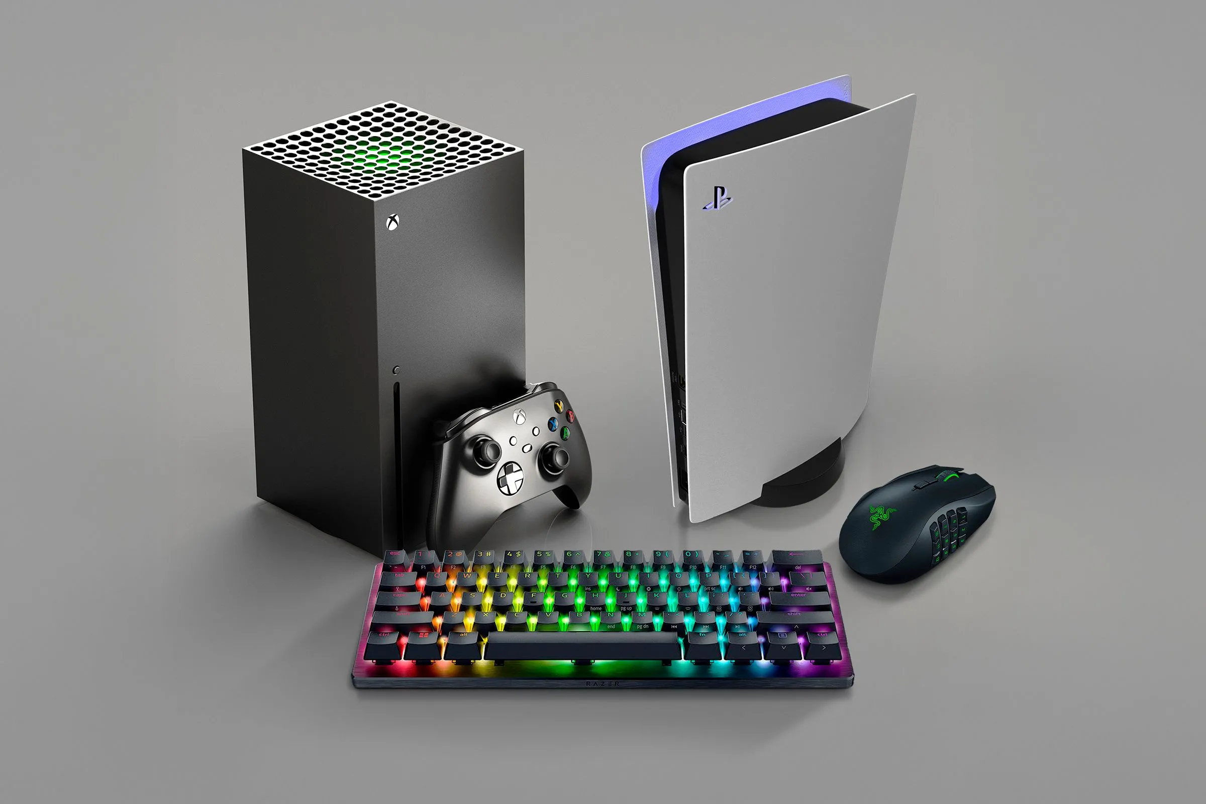 Một chiếc Xbox Series X đặt cạnh PlayStation, với bàn phím và chuột chơi game đặt kế bên, minh họa khả năng kết nối thiết bị ngoại vi