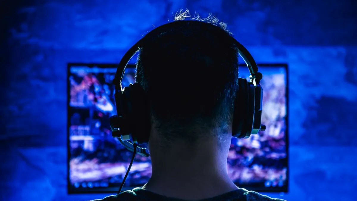 Một người đàn ông đang chơi game với tai nghe có dây trong môi trường tối, minh họa sự khác biệt giữa thói quen lành mạnh và phiên chơi game đêm mất kiểm soát.