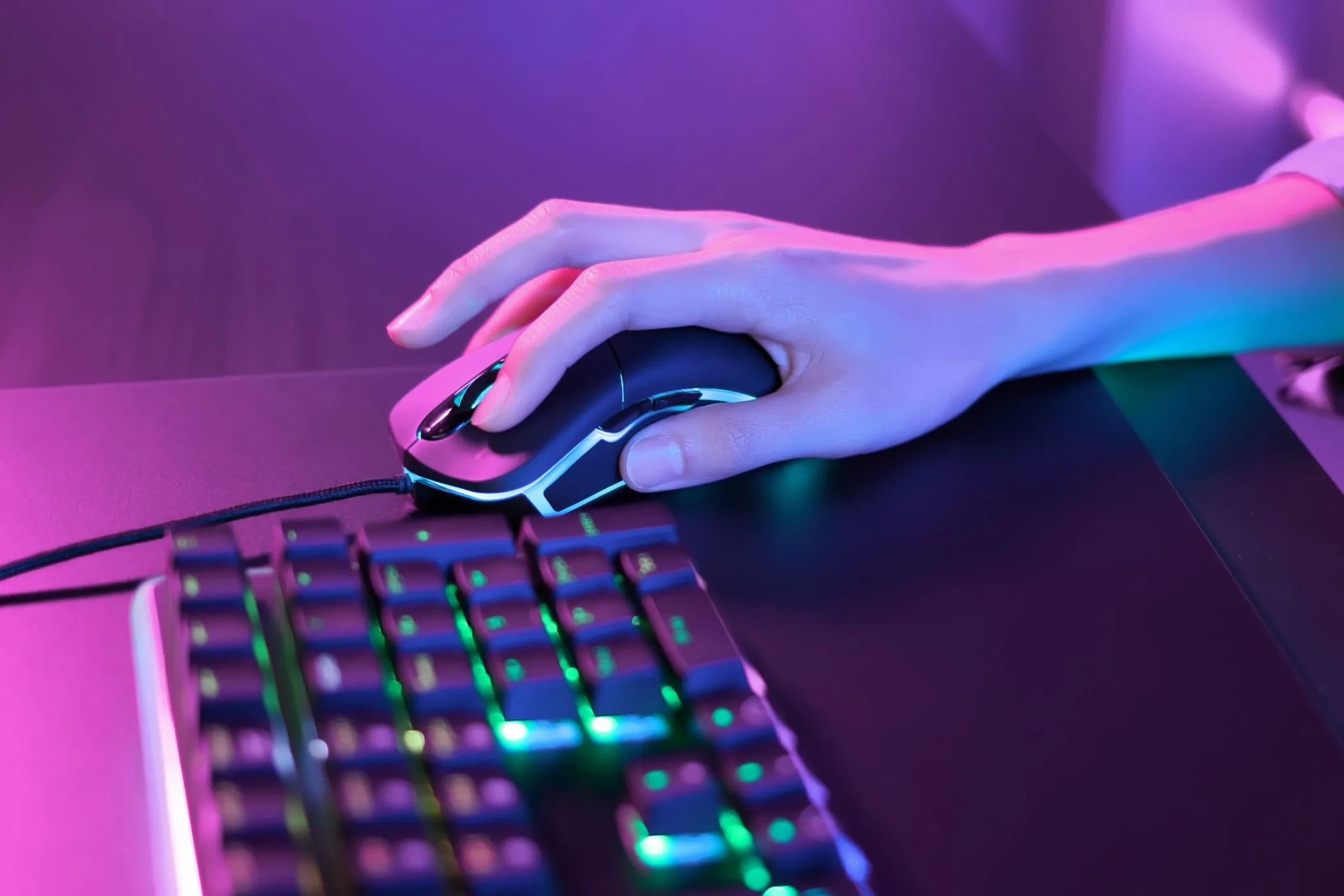 Một người đang sử dụng chuột gaming dưới ánh đèn neon hồng cạnh bàn phím RGB, thể hiện sự thư giãn và thoải mái khi chơi game.