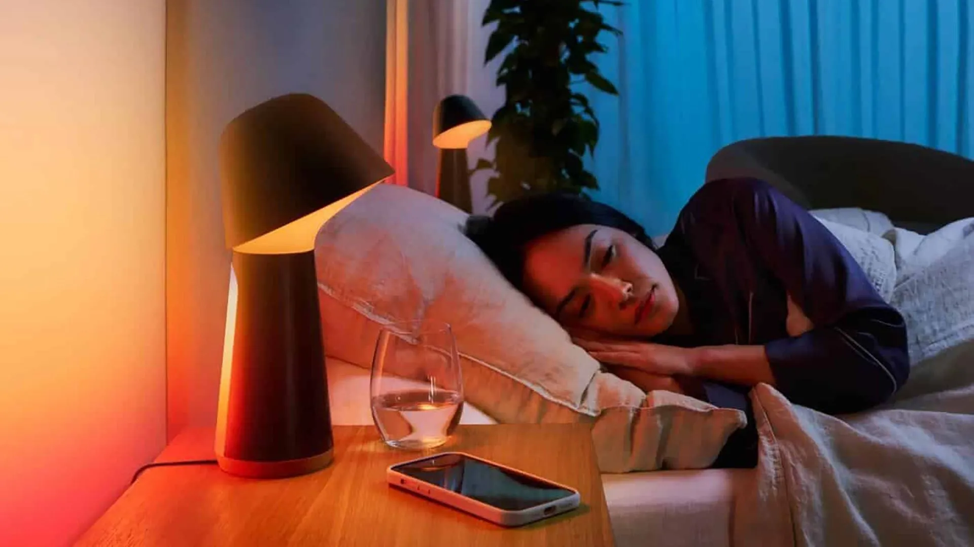 Người phụ nữ đang ngủ bên cạnh đèn thông minh và điện thoại, gợi ý việc dành thời gian suy nghĩ kỹ trước khi quyết định nâng cấp