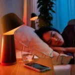 Người phụ nữ ngủ ngon giấc với điện thoại thông minh và đèn ngủ thông minh, thể hiện sự thư giãn nhờ tiếng ồn trắng.