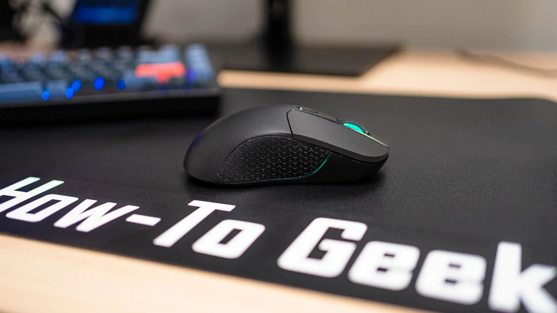 Chuột gaming không dây Keychron M3 màu đen trên tấm lót bàn How To Geek, thể hiện khả năng di chuyển mượt mà trên bề mặt lót chuột cứng hoặc kính.