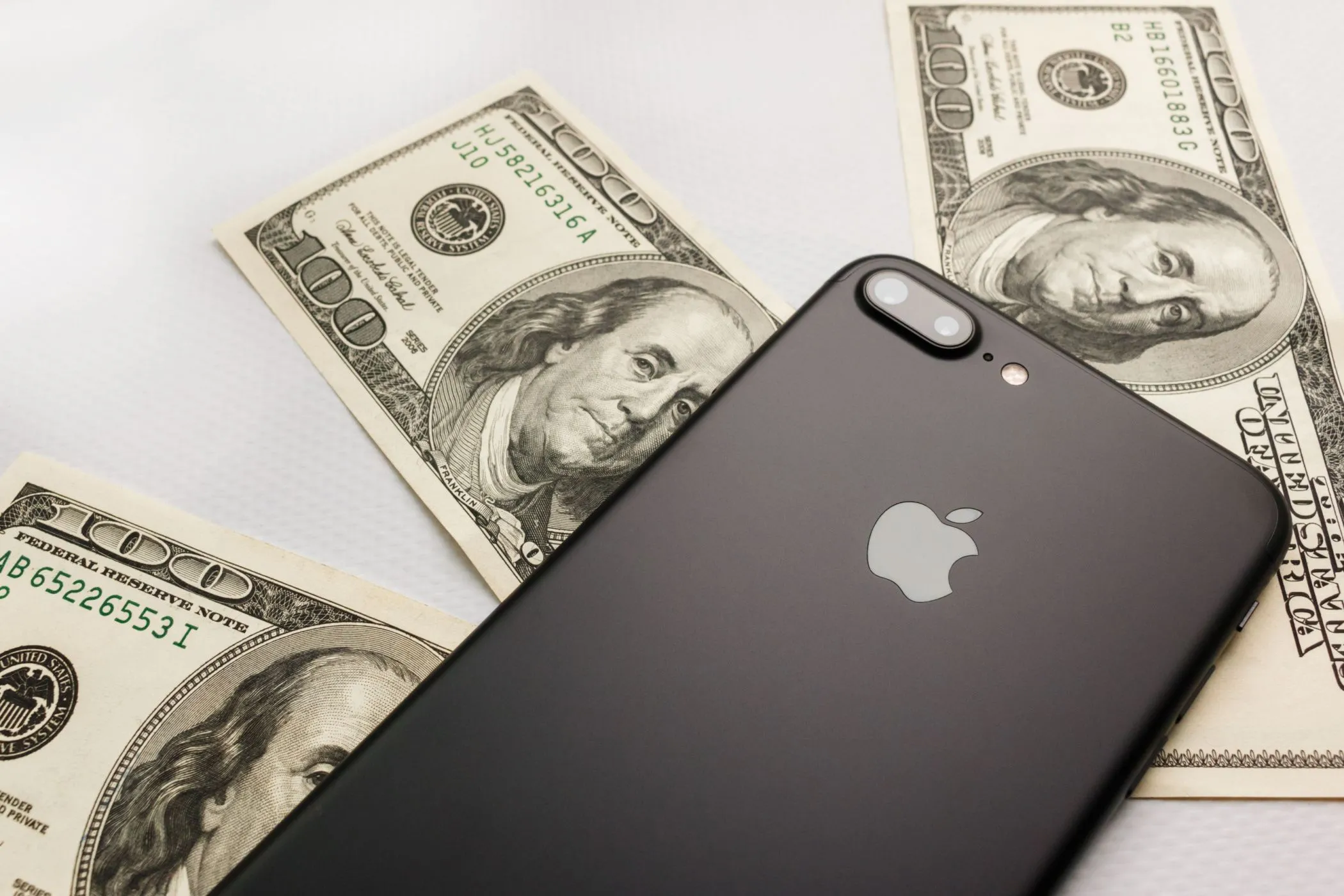 Điện thoại iPhone 8 Plus màu đen đặt trên xấp tiền đô la, biểu trưng cho chi tiêu game gacha không kiểm soát.