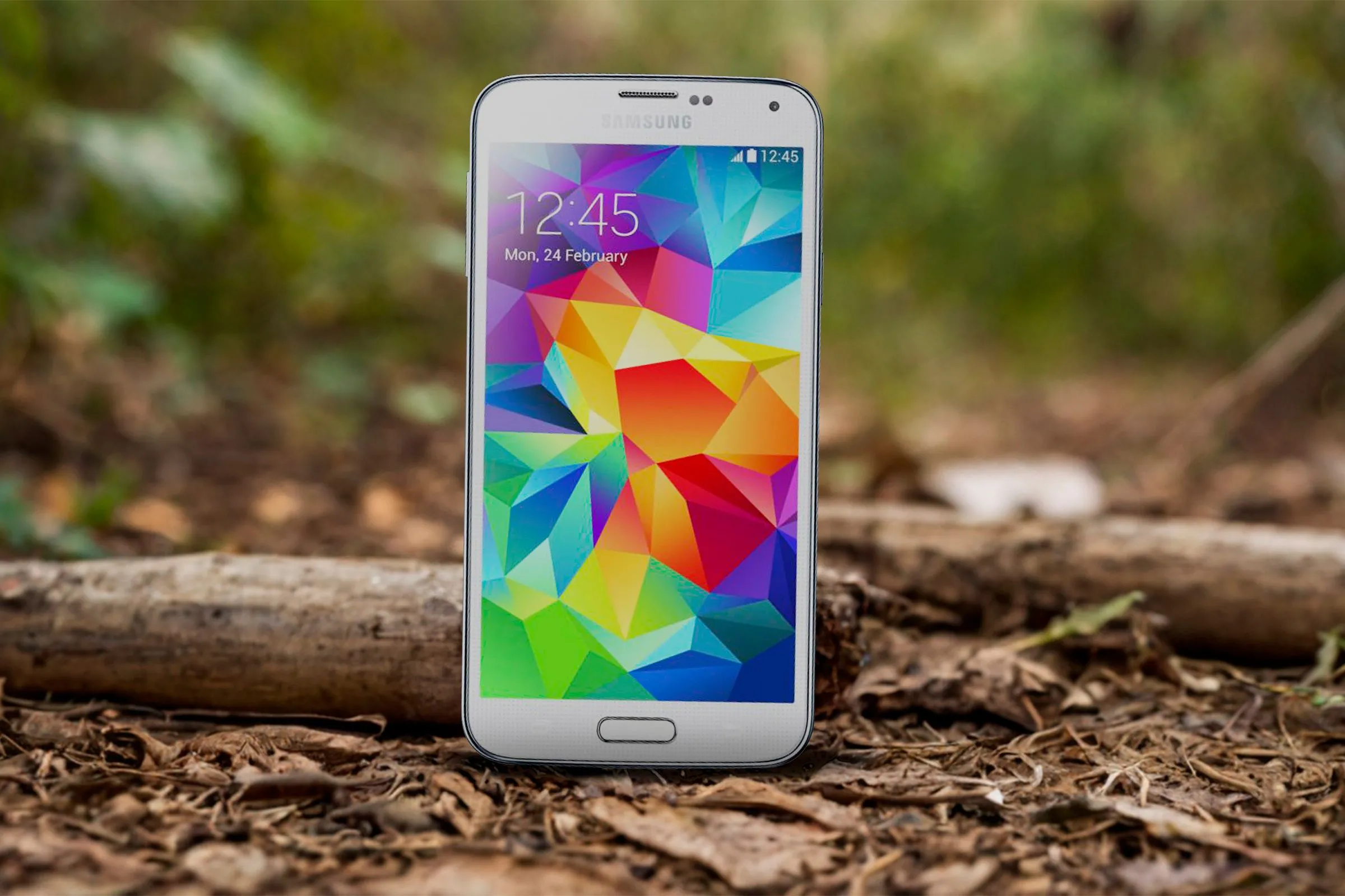 Điện thoại Samsung Galaxy S5 màu trắng nằm trên nền đất, minh họa thiết kế cũ bằng nhựa