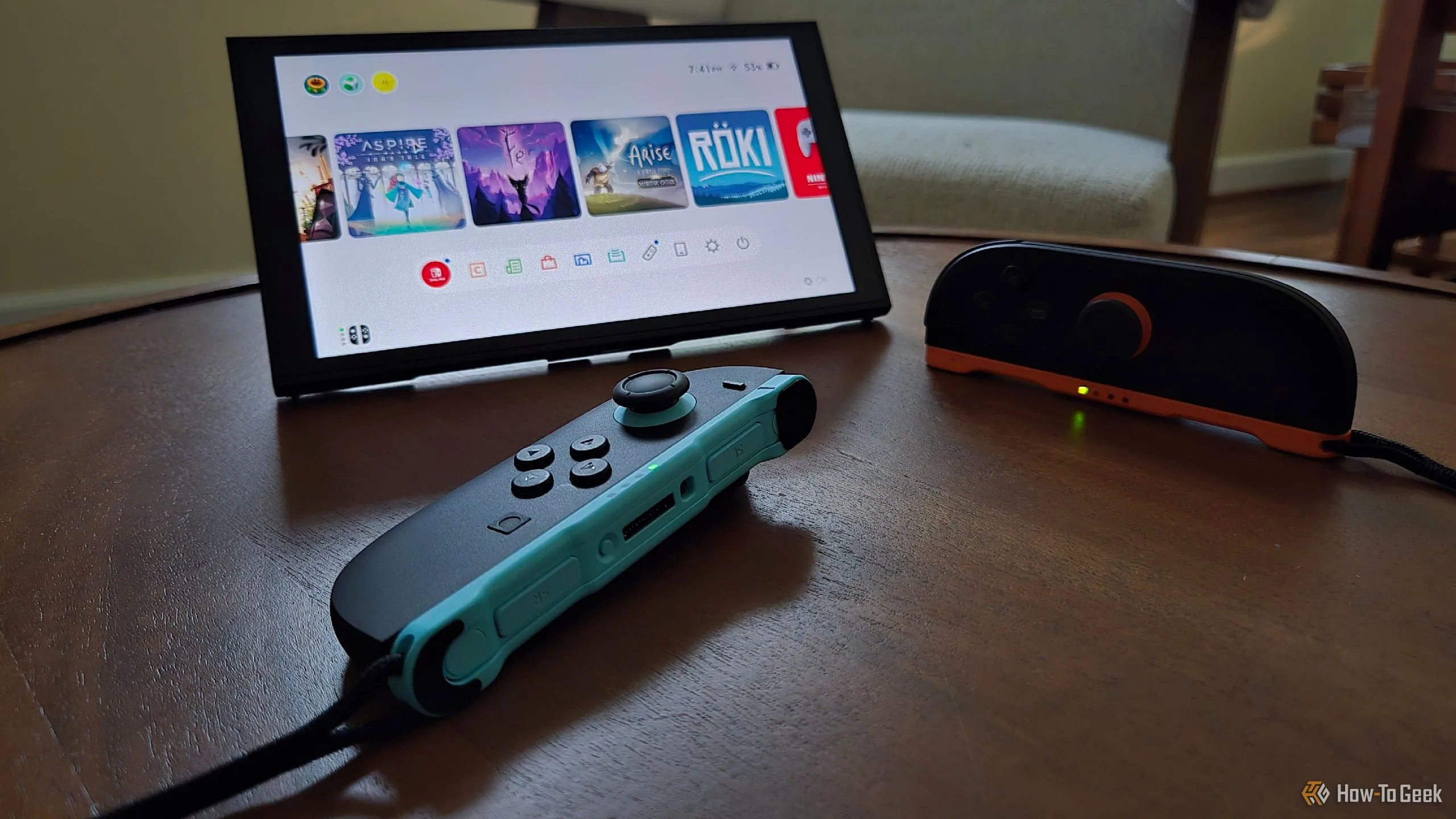 Hai tay cầm Joy-Con 2 đặt trước một máy Nintendo Switch 2 đang đứng trên chân đế tích hợp, hiển thị giao diện game indie.