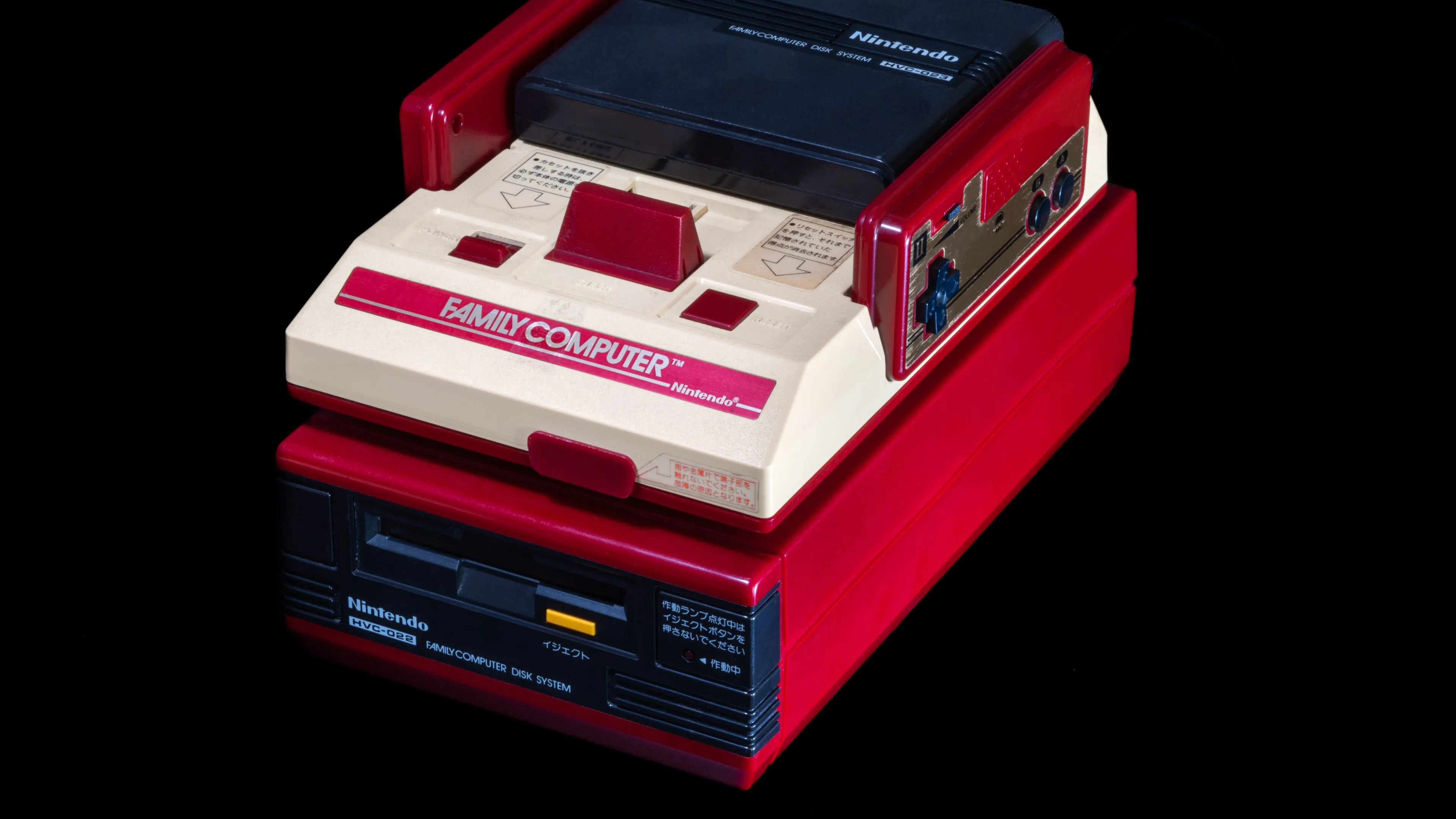 Hệ máy Nintendo Famicom kết nối với phụ kiện Famicom Disk System (FDS) màu vàng, mở rộng khả năng chơi game