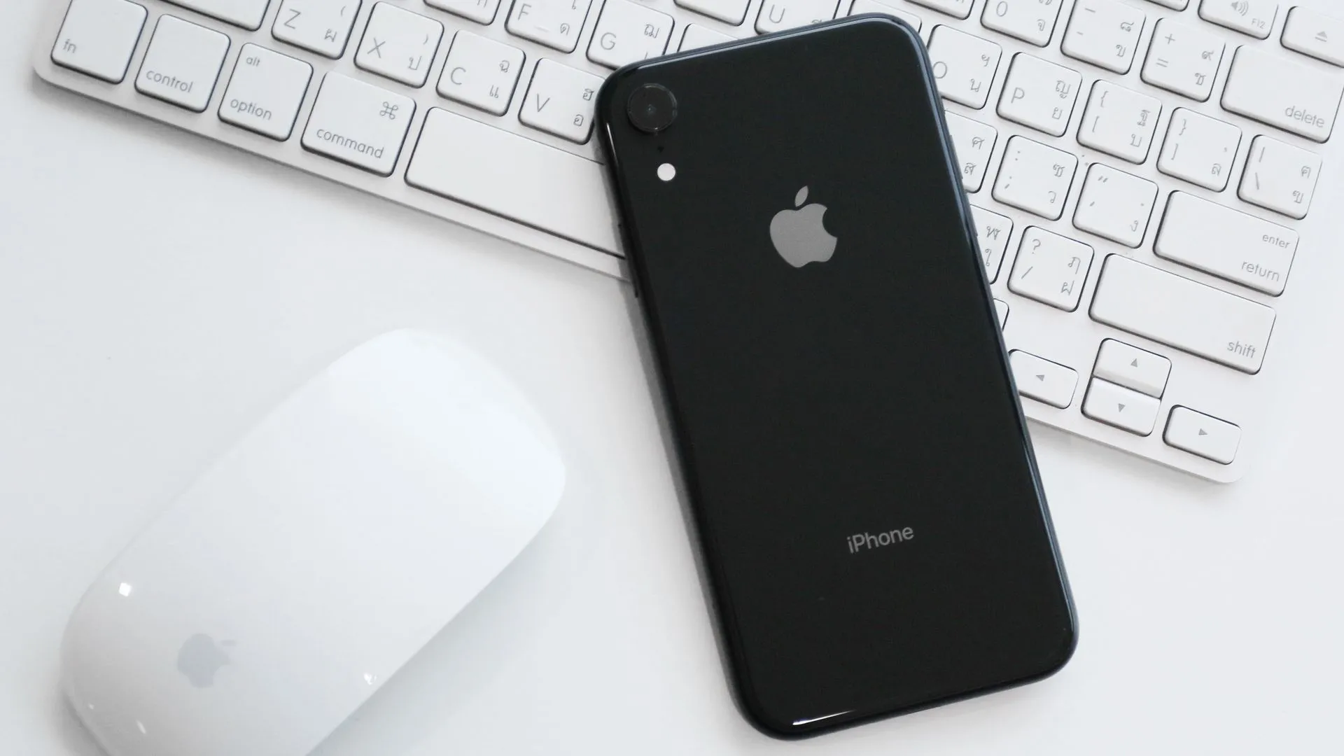 iPhone XR màu vàng trên bàn cùng Magic Mouse và Magic Keyboard, tượng trưng cho sự đơn giản và hiệu quả của camera đơn.
