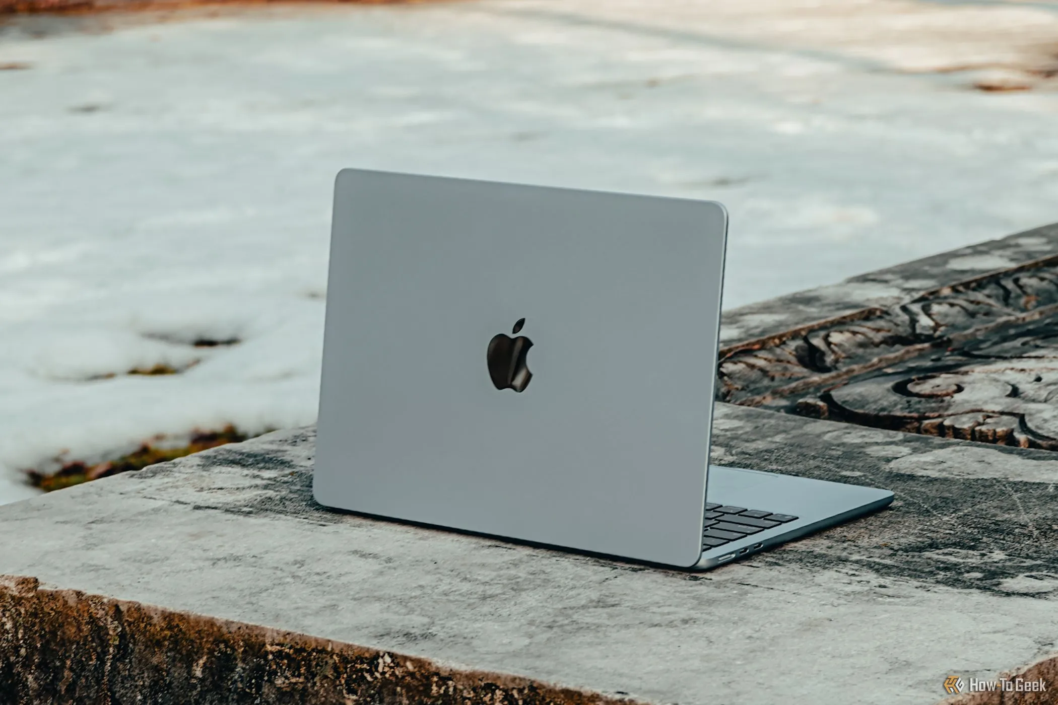 MacBook Air M4 màu xanh da trời đặt nghiêng trên một băng ghế bê tông, thể hiện thiết kế sang trọng.