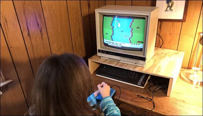 Một đứa trẻ đang chơi game River Raid trên máy tính Atari 800XL, thể hiện đồ họa pixel art đặc trưng của thời kỳ đầu game.
