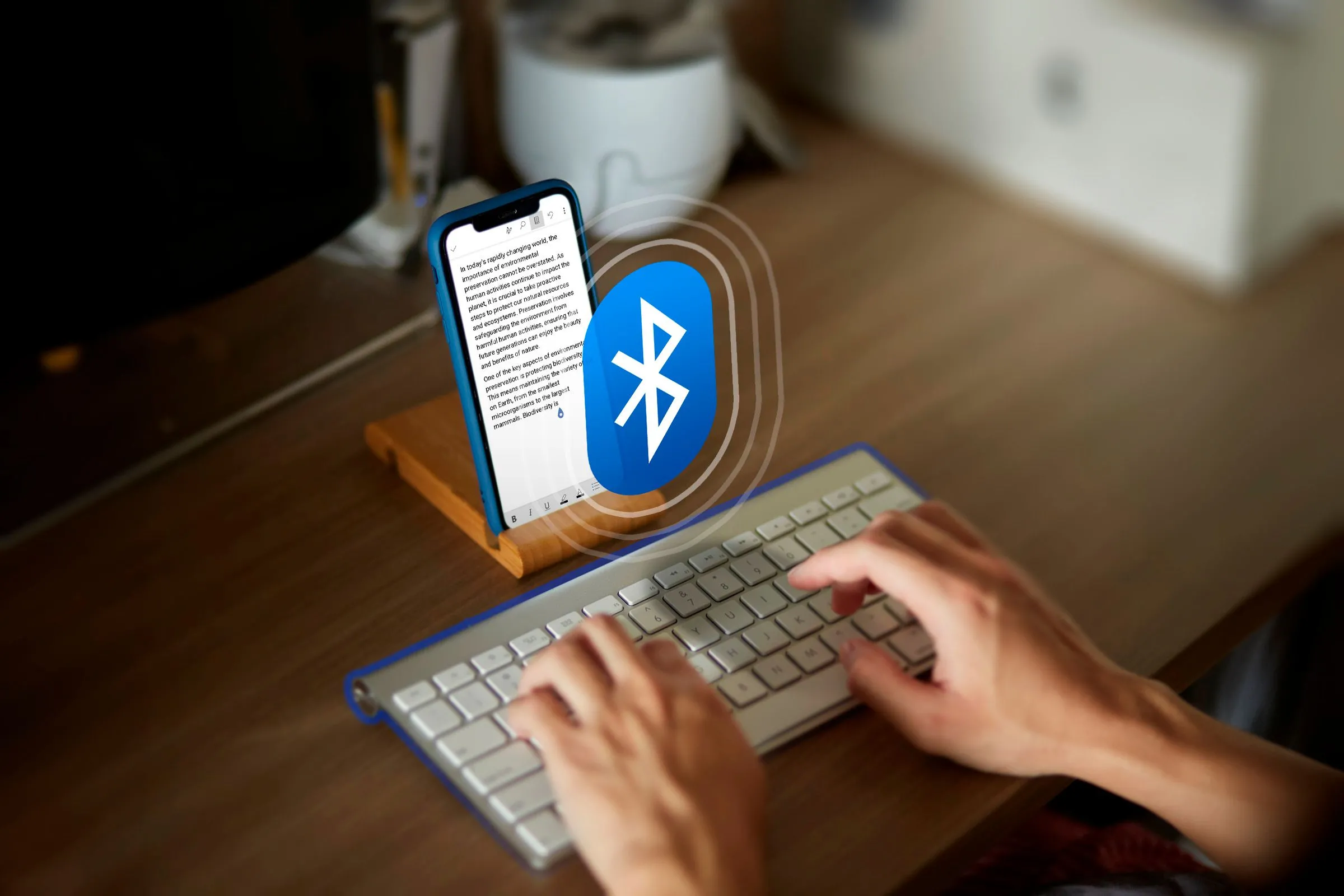Một người đang gõ văn bản trên điện thoại bằng bàn phím Bluetooth, với biểu tượng Bluetooth ở giữa.