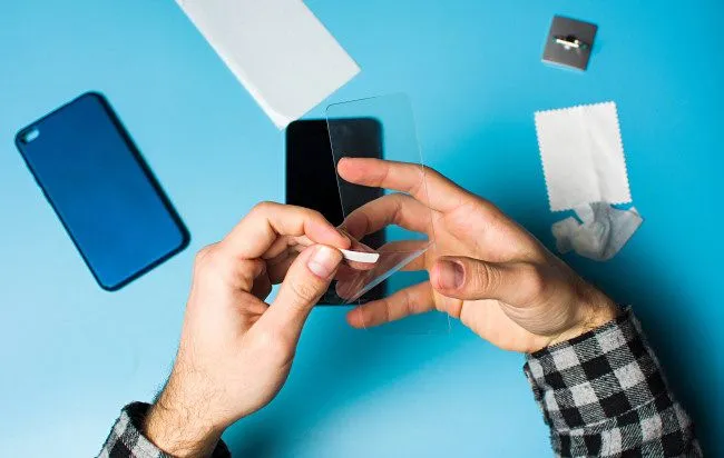 Người đàn ông đang dán miếng bảo vệ màn hình lên một chiếc iPhone với màn hình phẳng