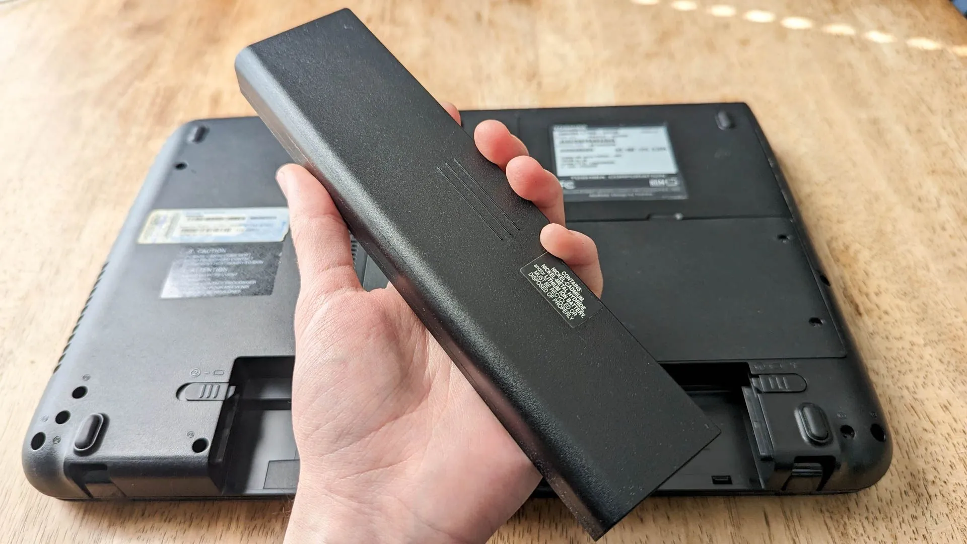 Người đang cầm một cục pin laptop có thể tháo rời