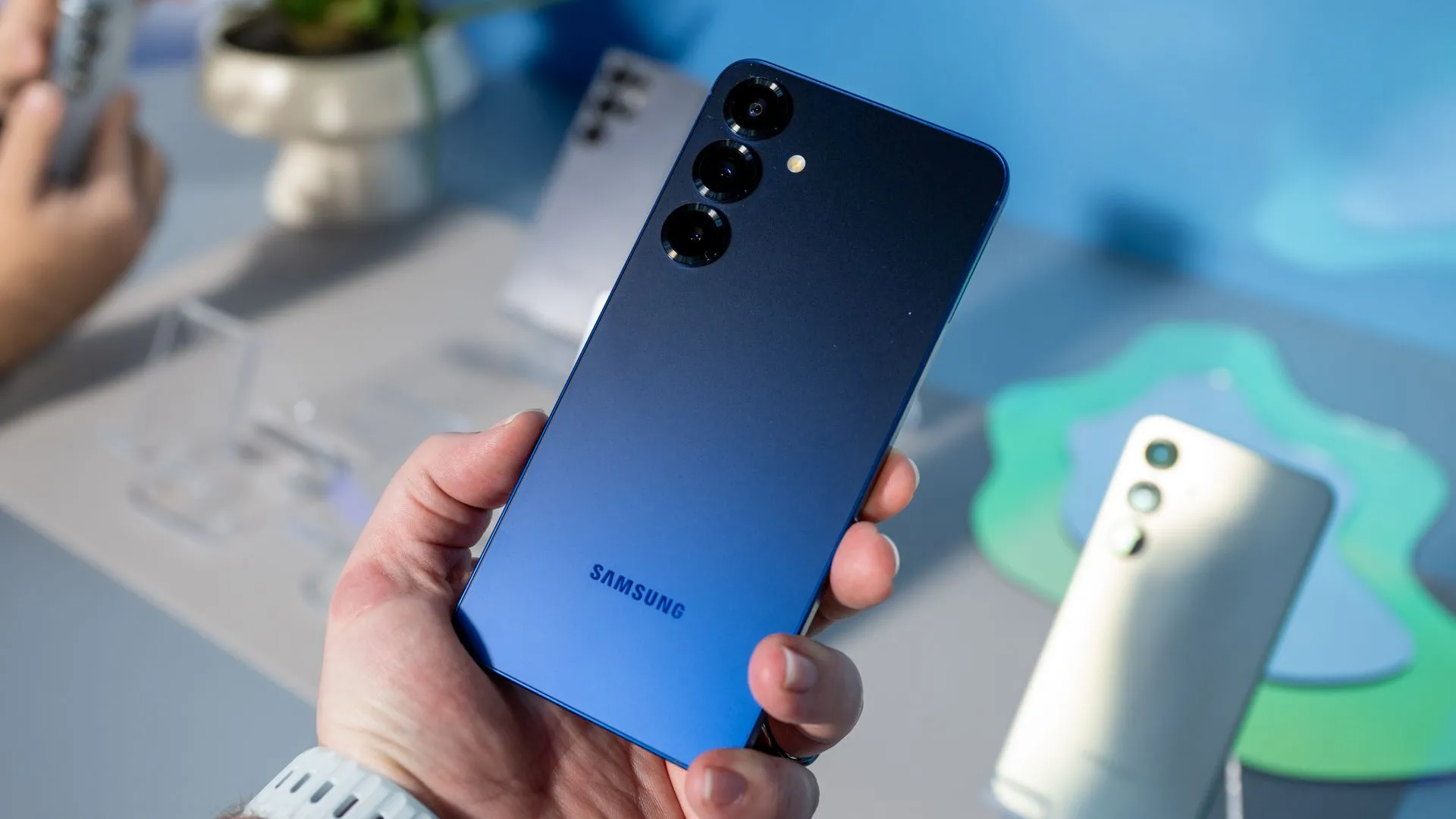 Người dùng đang cầm chiếc Samsung Galaxy S25 màu Xanh Navy, tôn lên thiết kế sang trọng và cụm camera ba ống kính
