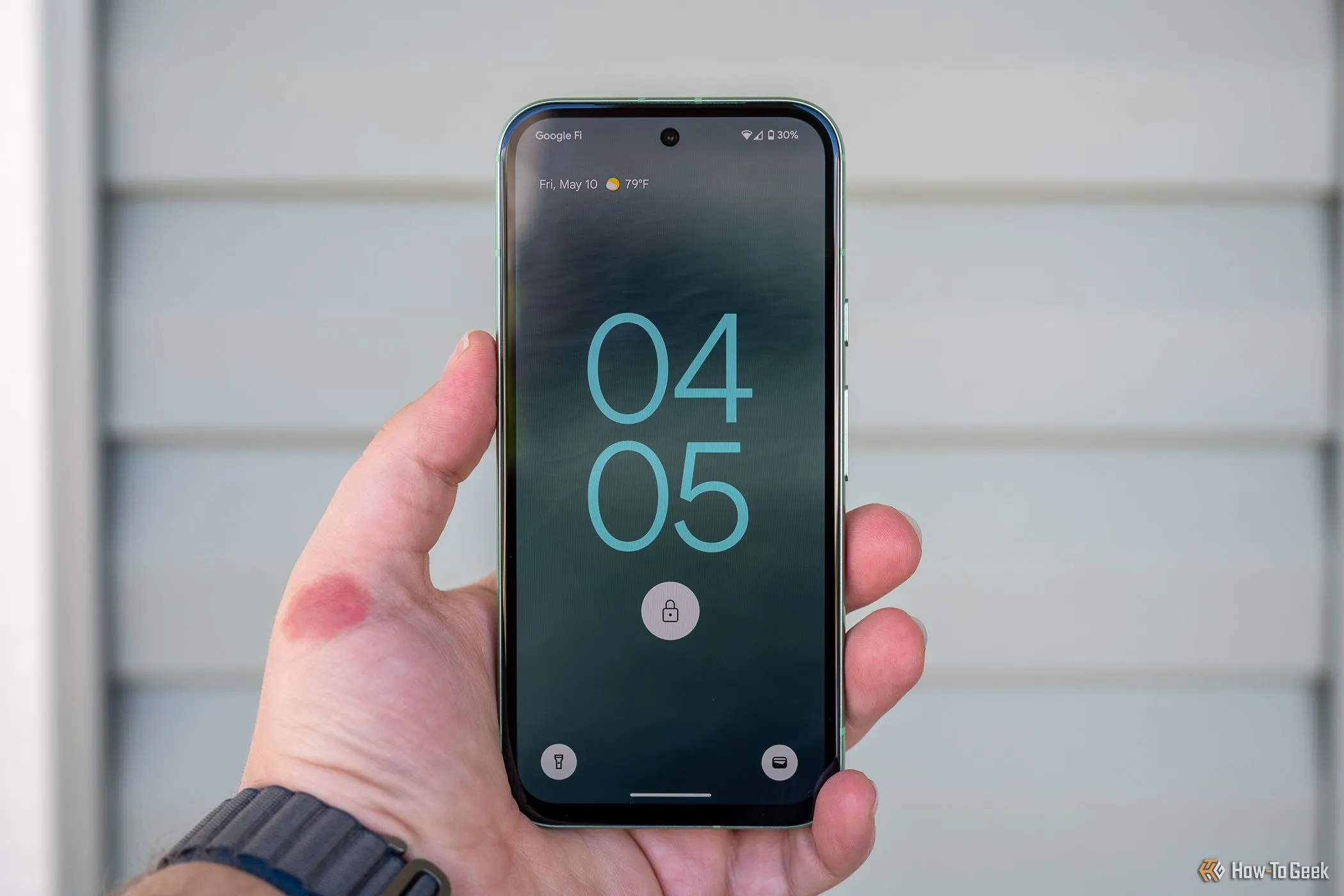 Người dùng đang cầm Google Pixel 8a hiển thị màn hình khóa