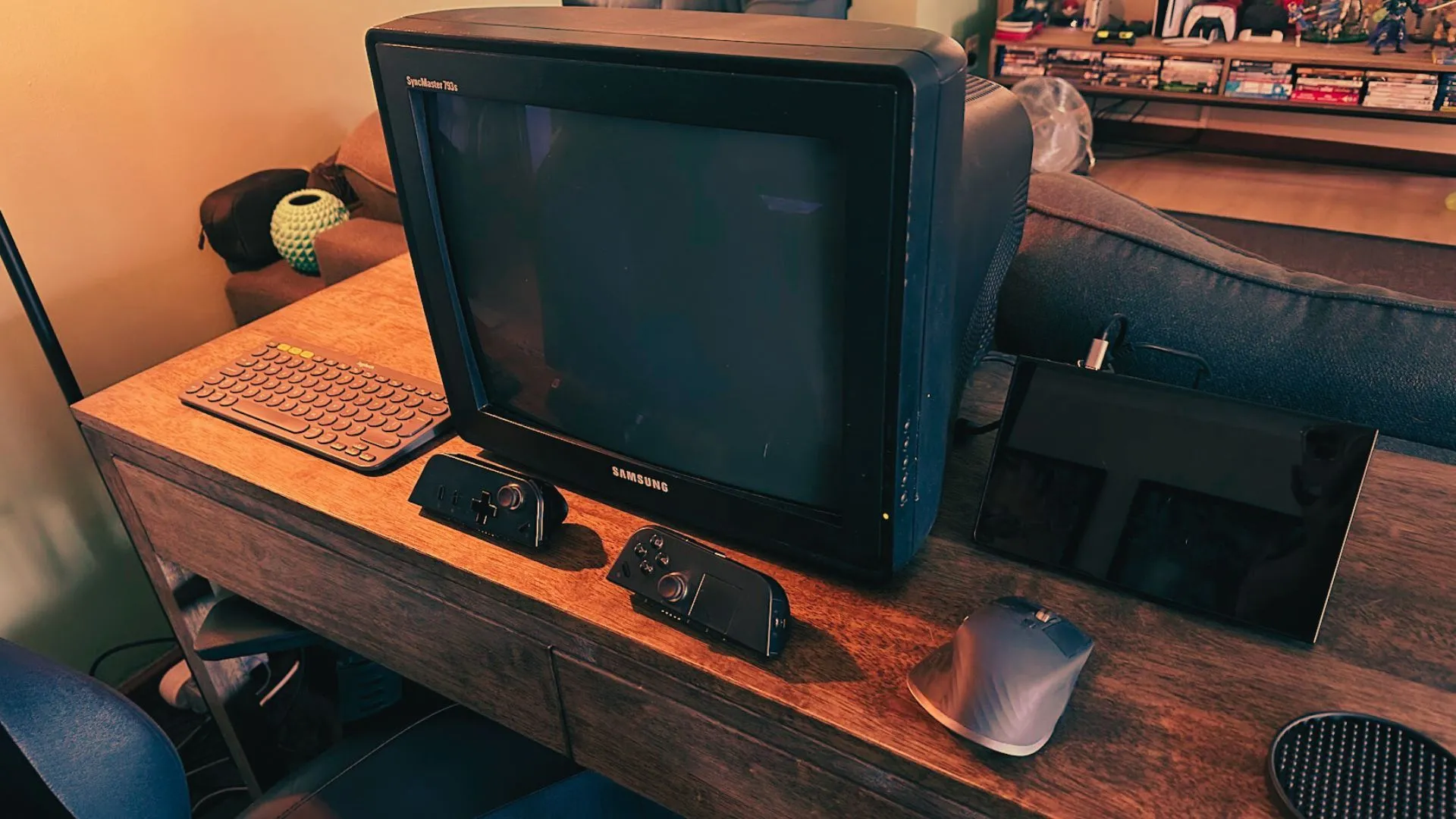 Thiết lập chơi game retro hoàn chỉnh với màn hình CRT, PC cầm tay, chuột, bàn phím và bộ điều khiển trên bàn làm việc.