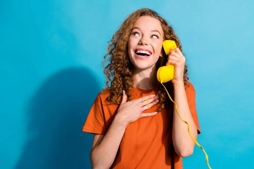 Một phụ nữ đang cầm chiếc điện thoại bàn màu vàng kiểu cũ